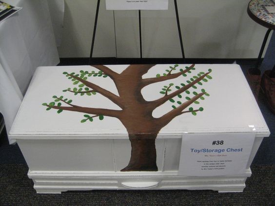 a cedar chest painted wihite with a tree used for a toybox