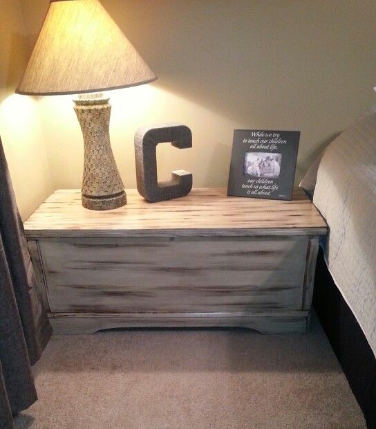 a distressed cedar chest sits beside a bed with a picture frame and lamp